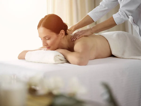 Ganska brunett kvinna njuter av proceduren med ryggmassage i solig spa salong. Skönhetsbegreppet — Stockfoto