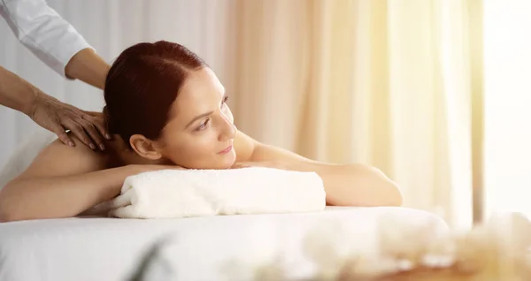 Pretty brunette woman enjoying procedure of back massage in sunny spa salon. Beauty concept — Stock Photo, Image