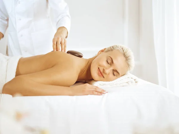 Hermosa mujer rubia disfrutando de piedras calientes procedimiento con los ojos cerrados. Concepto Spa — Foto de Stock