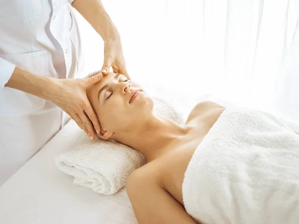 Hermosa mujer rubia disfrutando de masaje facial con los ojos cerrados. Tratamiento relajante en conceptos de medicina y centro de spa — Foto de Stock