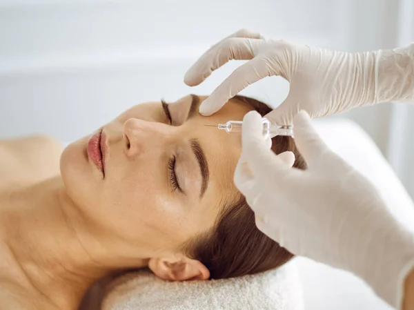 Beautician doing beauty procedure with syringe to face of young brunette woman. Cosmetic medicine and surgery, beauty injections