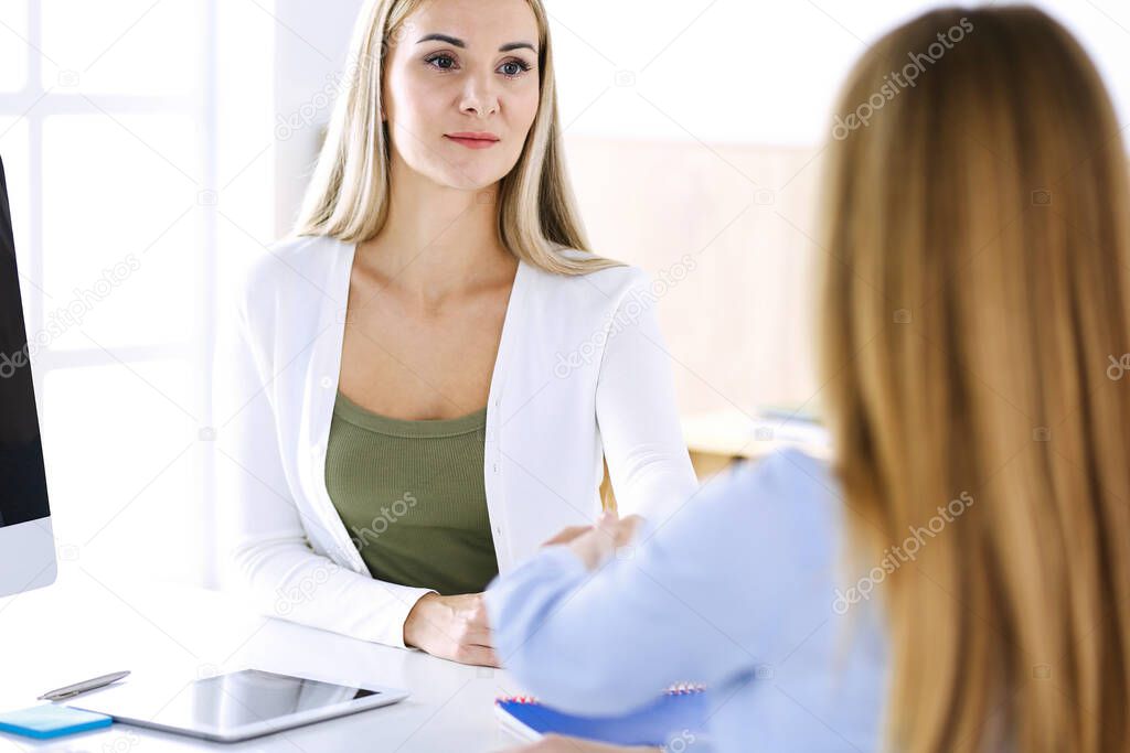 Business woman headshot while shaking hands with her female colleague or client in office. Casual white clothes style of business people. Audit, tax or lawyer concept