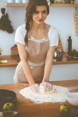 Genç esmer kadın mutfakta pizza ya da el yapımı makarna pişiriyor. Ev hanımı ahşap masada hamur hazırlıyor. Diyet, gıda ve sağlık konsepti