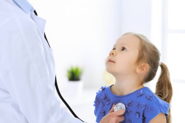 Doktor steteskopla küçük bir kızı muayene ediyor. Her zamanki tıbbi muayenede gülümseyen çocuk hasta. Tıp ve sağlık hizmetleri kavramları