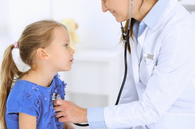 Doktor steteskopla küçük bir kızı muayene ediyor. Her zamanki tıbbi muayenede gülümseyen çocuk hasta. Tıp ve sağlık hizmetleri kavramları