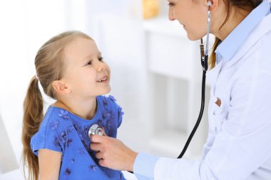 Doktor steteskopla küçük bir kızı muayene ediyor. Her zamanki tıbbi muayenede gülümseyen çocuk hasta. Tıp ve sağlık hizmetleri kavramları