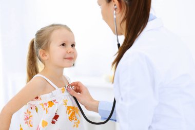 Doktor steteskopla küçük bir kızı muayene ediyor. Her zamanki tıbbi muayenede gülümseyen çocuk hasta. Tıp ve sağlık hizmetleri kavramları