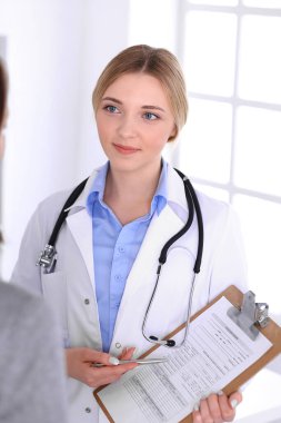 Hastane muayenehanesindeki genç kadın doktor ve hasta. Terapistin mavi renkli bluzu iyi görünüyor. Tıp ve sağlık hizmetleri kavramı