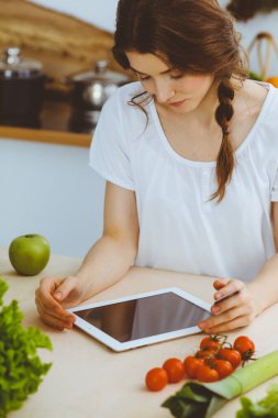 Genç bir kadın mutfakta yemek pişirmek için yeni bir tarif arıyor. Ev hanımı tablet bilgisayar ve kredi kartıyla online alışveriş yapıyor.