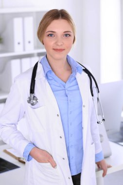 Hastanedeki genç kadın doktor kameraya bakıyor. Mavi renkli terapist bluzu iyi görünüyor. Tıp ve sağlık hizmetleri kavramı