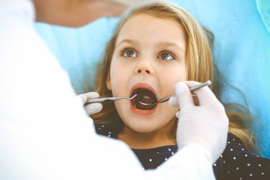 Doktor muayenesi sırasında ağzı açık bir şekilde dişçi koltuğunda oturan küçük kız. Dişçi muayenehanesi. Tıp konsepti. Renkli fotoğraf