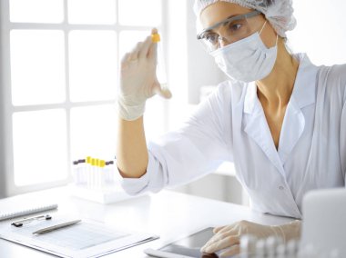 Koruyucu gözlüklü profesyonel kadın bilim adamı laboratuarda reaktörlerle araştırma tüpü kullanıyor. Tıp ve araştırma kavramları