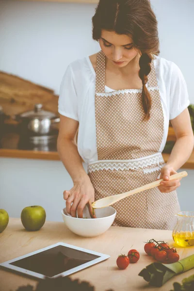 Mulher morena jovem cozinhar na cozinha. Dona de casa segurando colher de madeira na mão. Conceito de alimentação e saúde — Fotografia de Stock