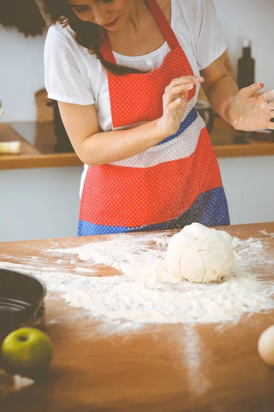 Jovem morena cozinhando pizza ou massa artesanal na cozinha. Dona de casa que prepara a massa de farinha na mesa de madeira. Conceito de alimentação, alimentação e saúde — Fotografia de Stock