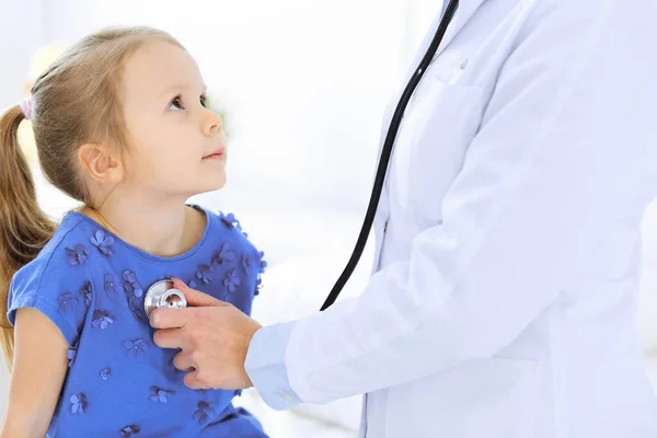 Lääkäri tutkii pikkutyttöä stetoskoopilla. Onnellinen hymyilevä lapsipotilas tavallisessa lääkärintarkastuksessa. Lääkkeiden ja terveydenhuollon käsitteet — kuvapankkivalokuva