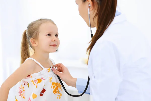 Arzt untersucht ein kleines Mädchen per Stethoskop. Glücklich lächelnder Kinderpatient bei der üblichen ärztlichen Untersuchung. Medizin- und Gesundheitskonzepte — Stockfoto