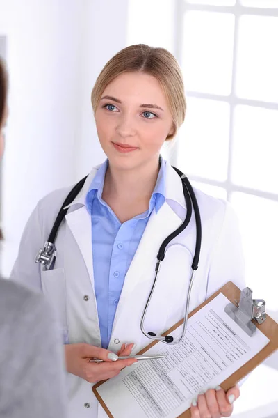 Молодая женщина врач и пациент при медицинском осмотре в больничном офисе. Синяя блузка терапевта выглядит хорошо. Медицина и здравоохранение — стоковое фото