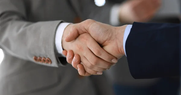 Business people shaking hands while standing with colleagues after meeting or negotiation, close-up. Group of unknown businessmen and women in modern office. Teamwork, partnership and handshake