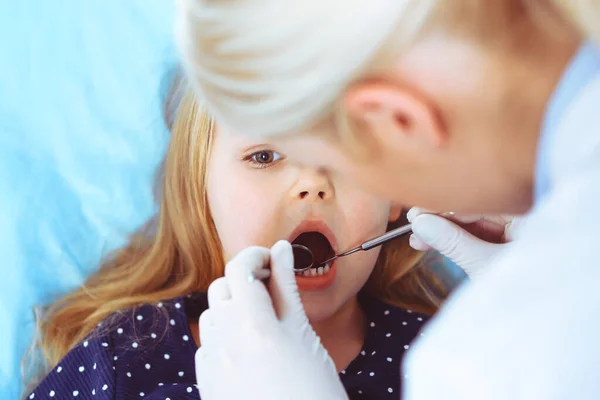 Kleine baby meisje zitten aan tandartsstoel met open mond tijdens orale check-up, terwijl de arts. Op bezoek bij de tandarts. Medicijnconcept. Getinte foto — Stockfoto