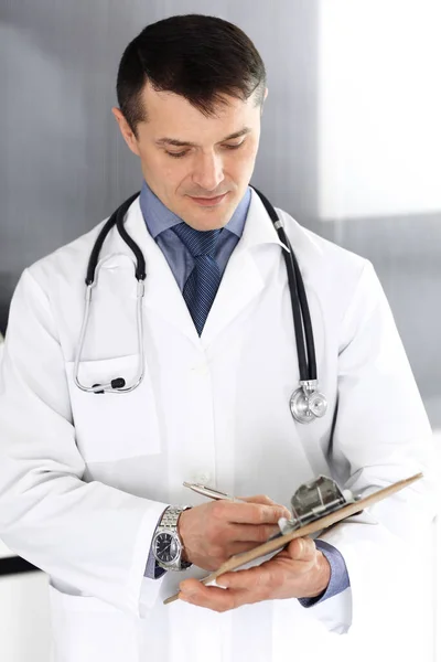 Dokter man met behulp van klembord voor het vullen van medicatie geschiedenis verslagen. Perfecte medische dienst in de kliniek. Artsen op het werk in het ziekenhuis. Begrippen geneeskunde en gezondheidszorg — Stockfoto