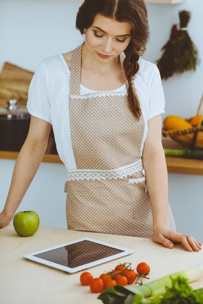 Young woman looking for a new recipe for cooking in a kitchen. Housewife is making online shopping by tablet computer and credit card