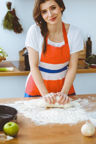 Jonge brunette vrouw koken pizza of handgemaakte pasta in de keuken. Huisvrouw maakt deeg op houten tafel. Dieet-, voedings- en gezondheidsconcept — Stockfoto