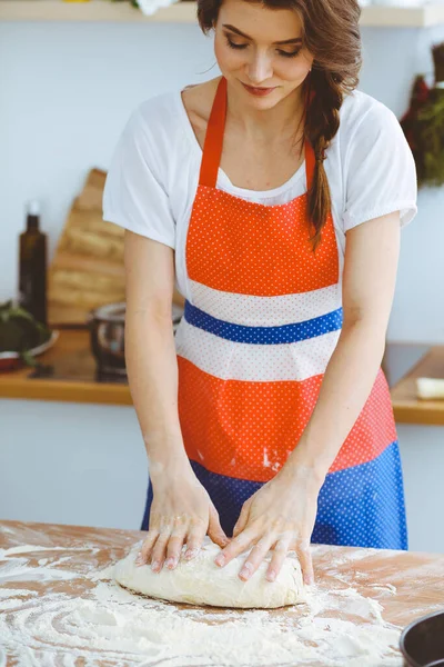 Jovem morena cozinhando pizza ou massa artesanal na cozinha. Dona de casa que prepara a massa de farinha na mesa de madeira. Conceito de alimentação, alimentação e saúde — Fotografia de Stock