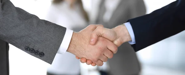 Business people shaking hands while standing with colleagues after meeting or negotiation, close-up. Group of unknown businessmen and women in modern office. Teamwork, partnership and handshake — Stock Photo, Image