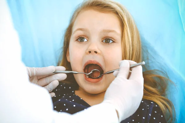 Malá holčička sedí u zubní židle s otevřenou pusou během orální prohlídky, zatímco doktor. Návštěva zubařské ordinace. Koncept medicíny. Izolovaná fotografie — Stock fotografie