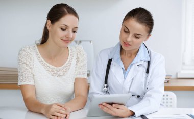 Doktor ve hasta tablet bilgisayar kullanırken oturup sağlık muayenesi sonuçlarını tartışıyorlar. Sağlık, ilaç ve iyi haber kavramları