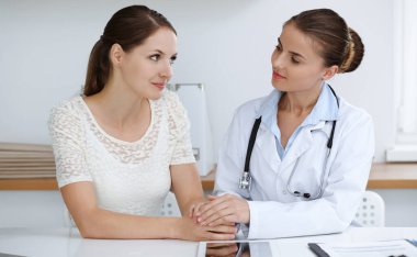 Kadın-doktor masasında otururken kadın hastasına güvence veriyor. Tıp konsepti