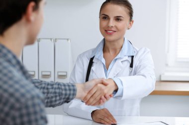 Kadın doktor, erkek hastasıyla tokalaşırken gülümsüyor. Tıp konsepti