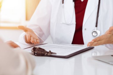 Bilinmeyen kadın doktor ve hasta güneşli klinikteki masada otururken bir şey tartışıyorlar.