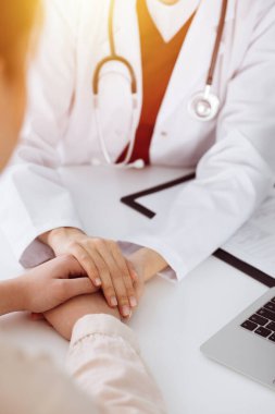 Kimliği belirsiz kadın doktorun elleri güneşli odada kadın hastasına güvence veriyor.