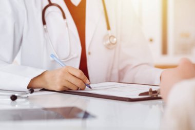Bilinmeyen kadın-doktor hastaya danışmanlık yaparken başvuru formu dolduruyor. güneşli oda tıp konseptinde