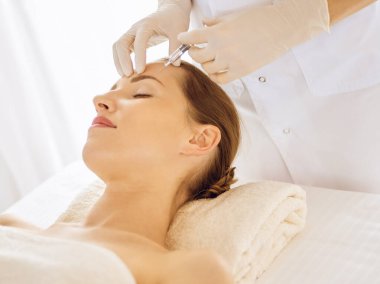 Güzel bir kadın kapalı gözlerle güzellik iğneleri yaptırıyor. Güzellik uzmanı elleri şırıngayla kadın yüzüne güzellik prosedürü uyguluyor.