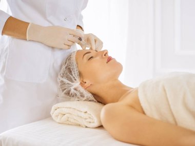 Güzel bir kadın kapalı gözlerle güzellik iğneleri yaptırıyor. Güzellik uzmanı elleri şırıngayla kadın yüzüne güzellik prosedürü uyguluyor.