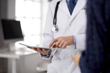 Dost canlısı kızıl sakallı doktor ve hasta kadın klinikte oturup tablet bilgisayar kullanırken sağlık muayenesini tartışıyorlar. Tıp konsepti