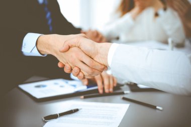 İş arkadaşları alkışlayıp alkışlarken iş adamları toplantıda tokalaşıyor. Modern beyaz ofisteki bir grup tanınmayan iş adamı ve kadın. Başarı takım çalışması, ortaklık ve tokalaşma