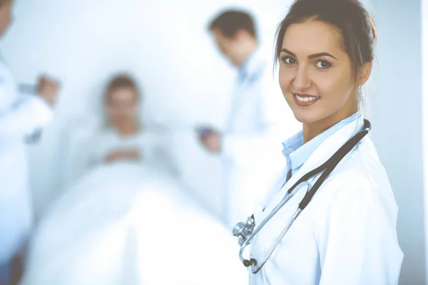 Female doctor smiling on the background with patient in the bed and two doctors