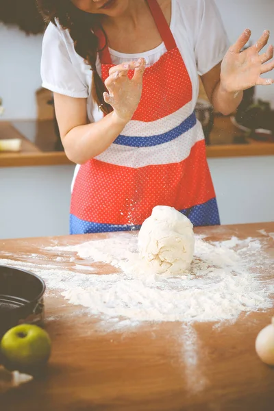 Jovem morena cozinhando pizza ou massa artesanal na cozinha. Dona de casa que prepara a massa de farinha na mesa de madeira. Conceito de alimentação, alimentação e saúde — Fotografia de Stock