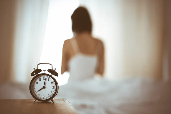 Woman stretching hands in bed after wake up, sun flare . Brunette entering a day happy and relaxed after good night sleep and back view. Concept of a new day and joyful weekend