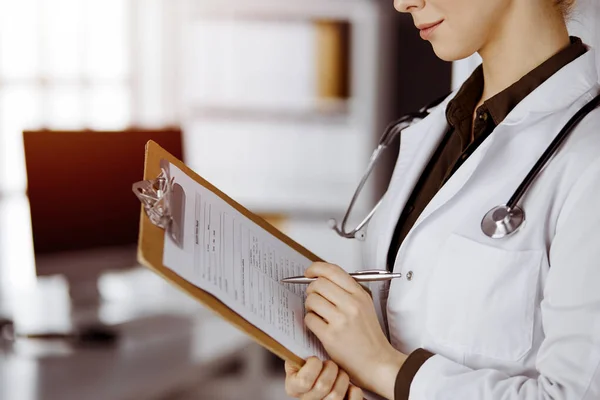 Médecin femme inconnue utilisant presse-papiers dans une clinique ensoleillée. Service médical parfait à l'hôpital — Photo