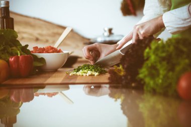 Mutfakta pişen bilinmeyen insan elleri. Yeşil soğan dilimleyen bir kadın. Sağlıklı yemek ve vejetaryen gıda konsepti.