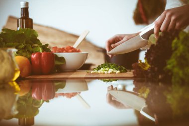 Mutfakta pişen bilinmeyen insan elleri. Yeşil soğan dilimleyen bir kadın. Sağlıklı yemek ve vejetaryen gıda konsepti.