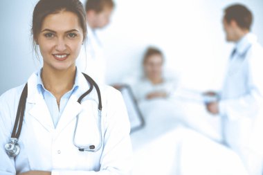 Arka planda gülümseyen kadın doktor, yatakta hasta ve iki doktor.