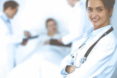 Arka planda gülümseyen kadın doktor, yatakta hasta ve iki doktor.