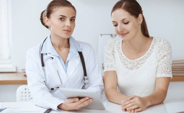 Doktor ve hasta tablet bilgisayar kullanırken oturup sağlık muayenesi sonuçlarını tartışıyorlar. Sağlık, ilaç ve iyi haber kavramları