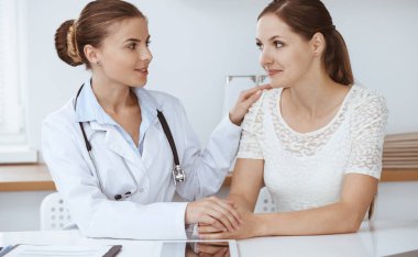 Kadın-doktor masasında otururken kadın hastasına güvence veriyor. Tıp konsepti