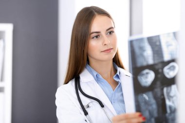 Doktor kadın hastanenin penceresinin yanında dikilirken röntgen filmini inceliyor. Cerrah ya da ortopedist. Tıp ve sağlık hizmetleri kavramı